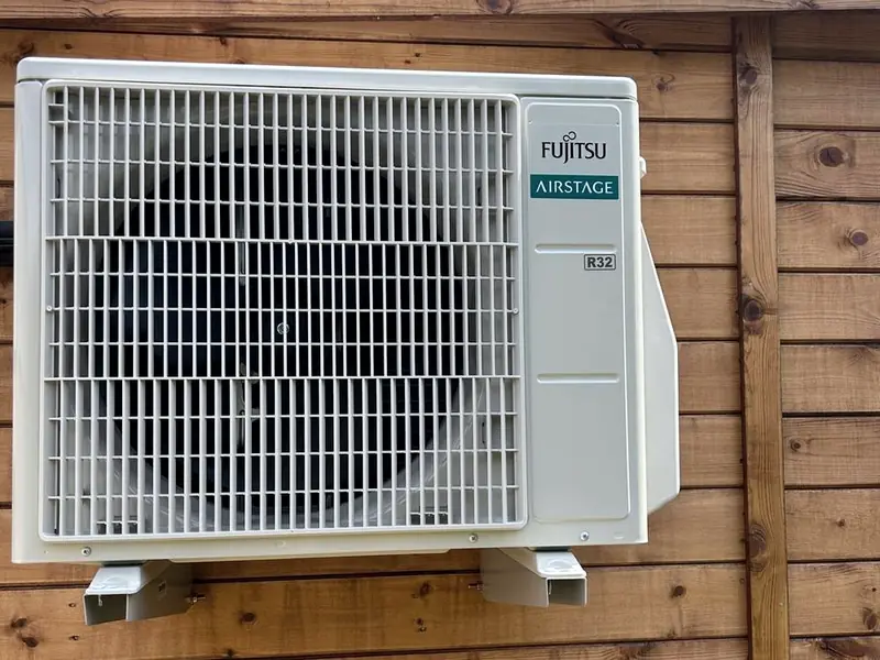 Air conditioning outdoor unit mounted on the timber wall of a garden office