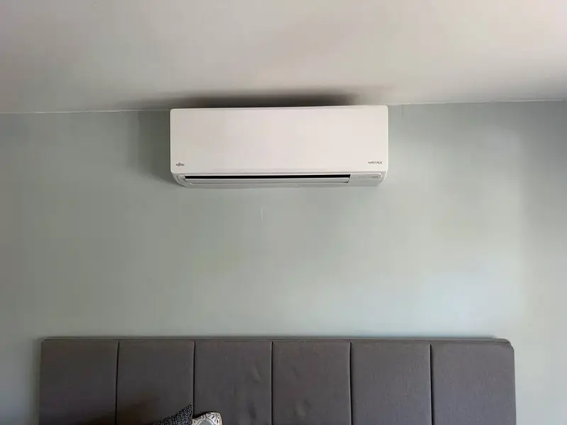 Slim white wall-mounted air conditioning unit above a bed